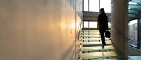 Professional businessman in suit climbing modern glass staircase in contemporary office building with natural lighting and urban architecture.