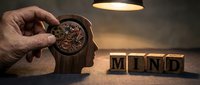 Adult male hand holding compass above wooden mug with gears inside, mind wooden blocks nearby, warm overhead lighting, conceptual composition for mindfulness and mental clarity themes.