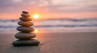 Zen stone stack on beach at sunset with golden sky reflection creating peaceful meditation and balance concept for wellness and mindfulness practices.