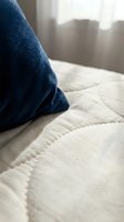 Close-up of navy blue fabric draped on white quilted bedding with soft natural light from window. Cozy bedroom interior design and home textile concept.