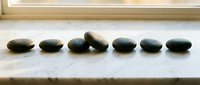Smooth dark stones arranged in a row on white surface near window, symbolizing balance, wellness, and meditation for spa, relaxation, and mindfulness content.