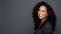 Portrait of a young woman with long, curly dark hair and warm smile, wearing dark sweater against neutral gray background. Suitable for business, lifestyle, and professional websites.
