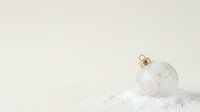 White frosted ornament with snowflake patterns resting on snow against neutral background, suitable for holiday greeting cards and seasonal marketing materials.