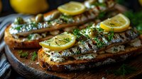 Grilled sardines on crusty bread with fresh herbs, lemon slices and olive oil served on rustic wooden board. Mediterranean appetizer in moody lighting.