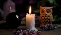 Mystical altar setup with burning candle, crystal ball, owl figurine and lavender herbs for spiritual practices, meditation and fortune telling rituals.