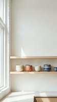 Minimalist kitchen interior with wooden floating shelves displaying ceramic bowls near bright window for modern home design and organization concepts.