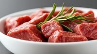 Raw beef chunks with fresh rosemary sprigs in white ceramic bowl, close up view of marbled red meat cuts ready for cooking, selective focus on meat texture.