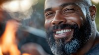 Smiling African American man with gray beard enjoying outdoor barbecue grilling experience with warm natural lighting and joyful expression.