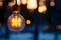 Glowing vintage filament bulb with decorative glass pattern against blurred warm bokeh background creates cozy atmospheric lighting mood.