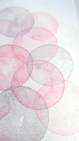 Abstract watercolor circles in soft pink and gray tones overlapping on white paper creating delicate translucent layers for modern artistic backgrounds.