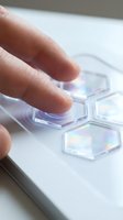 Hand touching holographic hexagonal interface elements with iridescent rainbow colors on white surface for futuristic technology and digital interaction concepts.