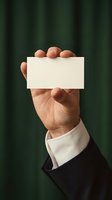 Professional businessman hand holding blank white business card against green curtain background for corporate branding and marketing materials.