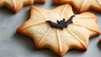 Star-shaped sugar cookie decorated with white icing lines and black bat detail on gray background, festive Halloween baked treat for holiday parties.