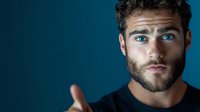 Young Caucasian male with blue eyes and beard looking intensely at camera against dark blue background, dramatic studio lighting creates mysterious mood.