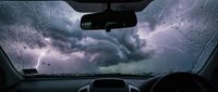 Dramatic storm clouds viewed from inside car with raindrops on windshield creating moody atmospheric driving scene for weather and transportation concepts.