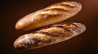Two fresh artisan baguettes with golden crusts and rustic scoring marks on warm brown background for bakery and food photography projects.