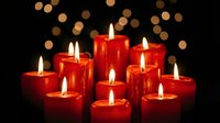 Red candles burning with warm flames creating cozy atmosphere against dark background with golden bokeh lights for holiday celebrations and romantic settings.