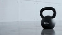 Black 24kg kettlebell on gym floor for strength training and fitness workouts in modern exercise facility with white tiled wall background.