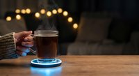 Steaming hot coffee mug held by hands in cozy sweater on glowing blue coaster with warm bokeh lights creating atmospheric evening ambiance for relaxation.