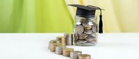 Graduation cap on glass jar filled with coins next to stacked money representing education savings fund and student financial planning concept.