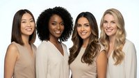 Four diverse professional women in neutral business attire smiling confidently at camera, representing teamwork and corporate success in modern workplace.