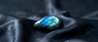 Luminous blue labradorite gemstone with iridescent flash resting on dark fabric creating mystical atmosphere for jewelry design and spiritual concepts.