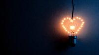 Glowing heart-shaped light bulb hanging against dark background creates romantic atmosphere, symbolizing love, creativity and bright ideas for Valentine's designs.