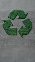 Green recycling symbol embroidered on gray fabric texture for sustainable fashion and eco-friendly clothing design concepts.