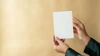 Hands holding blank white paper sheet against neutral beige wall background, mockup for branding, advertising, and marketing materials.