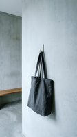 Minimalist dark gray linen tote bag hanging on white concrete wall hook in modern interior space for sustainable shopping and everyday use.