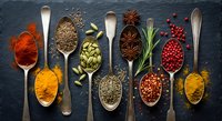 Colorful spices and herbs arranged in vintage wooden spoons on dark slate background. Culinary ingredients for cooking and seasoning food preparation.