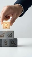 Businessman hand placing wooden cube with lightbulb icon on stack of business symbol blocks representing innovation and strategic growth planning.