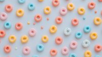 Colorful glazed donuts in pastel pink, blue, yellow and white scattered on light blue background creating playful pattern for food industry and packaging design.