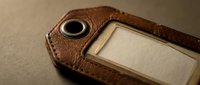 Vintage brown leather luggage tag with blank label and metal grommet, close-up macro shot on dark background for travel and retail concepts.
