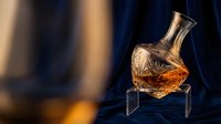Crystal whiskey decanter with amber liquid on glass stand against blurred warm background. Luxury barware for home bar and entertaining.