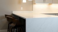 Modern kitchen interior with white marble countertop and dark wooden bar stools under pendant lighting for contemporary home design and renovation projects.
