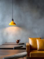 Modern cafe interior with yellow pendant lamp illuminating wooden table, leather sofa and concrete wall creating cozy minimalist atmosphere for restaurant design.