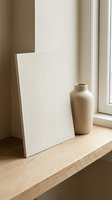 Minimalist interior scene with blank canvas and ceramic vase on wooden shelf by window. Natural lighting creates warm shadows for home decor and art display.