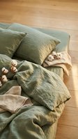 Sage green linen bedding set with cotton branch decoration on wooden floor creating cozy natural bedroom interior for home decor and textile design.
