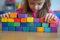 Young girl in pink shirt arranging colorful wooden blocks in a row on wooden table, focused on creative play and early childhood development activities.