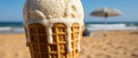 Vanilla ice cream melting on waffle cone at sandy beach with ocean and umbrella in background, summer dessert and vacation concept.