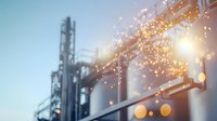 Industrial manufacturing plant with bright sparks and bokeh lights against blue sky at dusk, metal structures and storage tanks creating dramatic atmosphere.