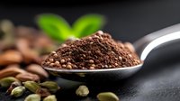 Ground coffee powder on metal spoon with roasted beans and cardamom pods scattered on dark background, fresh mint leaves add natural accent. Food photography.