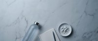 Minimalist workspace with blue water bottle, white notebook, pen and small bowl on elegant marble surface for productivity and wellness lifestyle.