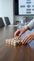 Business professional arranging wooden blocks with house icons on conference table during strategic planning meeting in modern office boardroom.
