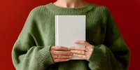 Young woman in green knitted sweater holding blank book against vibrant red background, showcasing minimalist design aesthetic for publishing or reading concepts.