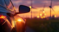 Modern car side mirror reflecting golden sunset sky with wind turbines silhouettes in background, dramatic evening atmosphere with bokeh lights.