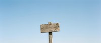 Weathered wooden signpost against clear blue sky background for rustic outdoor advertising and directional messaging concepts.