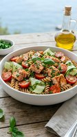 Fresh salmon pasta salad with cherry tomatoes, cucumber, and herbs in a white bowl on a wooden table by the sea.