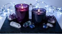 Purple and dark candles burning with healing crystals amethyst quartz on slate board surrounded by fairy lights for meditation spa wellness ritual.